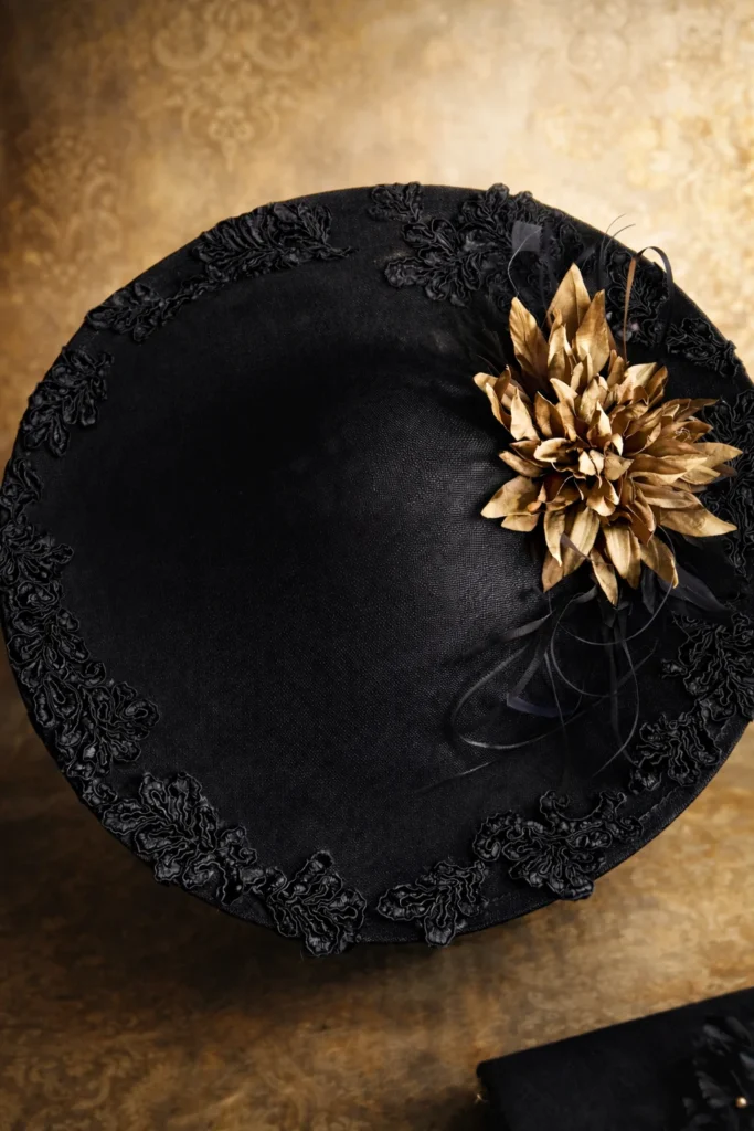 Detalle de pamela negra con flor dorada, aplicaciones de guipur y plumas artesanales