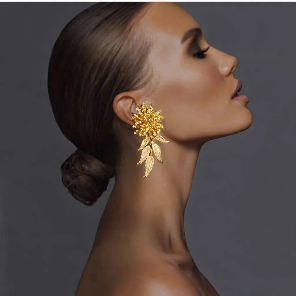 Detalle de pendientes dorados artesanales con rosetón de cuentas y hojas